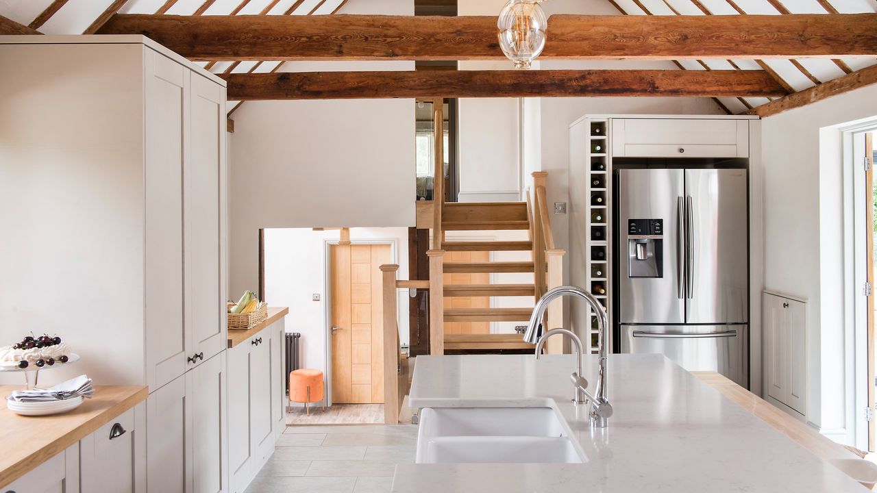 A large kitchen with high ceiling and exposed beams and a silver fridge