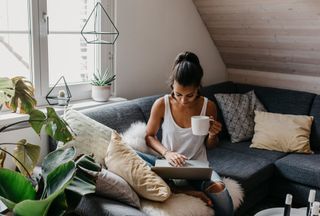 young woman working from sofa in apartment surrounded by plants