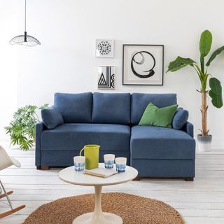 A blue corner sofa bed in a white living room with a circular brown woven rug on the floor