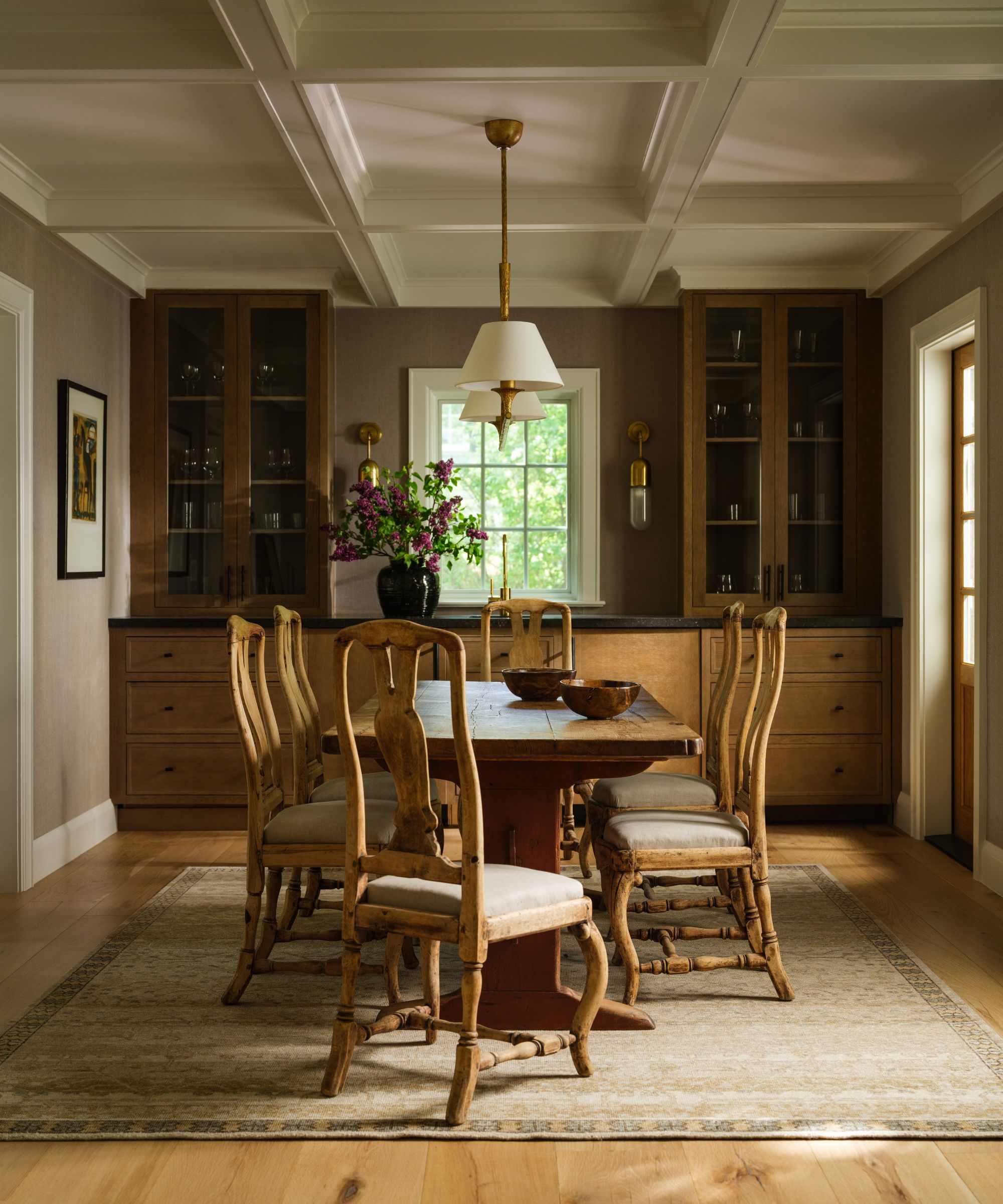 a warm neutral dining room with custom wooden bar and storage, mixed wooden vintage table and chairs and a coffered ceiling