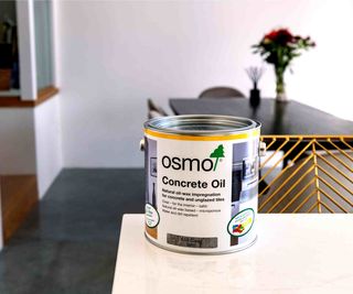 A tin of Osmo concrete oil on top of a white kitchen worktop, with a dining table in the background