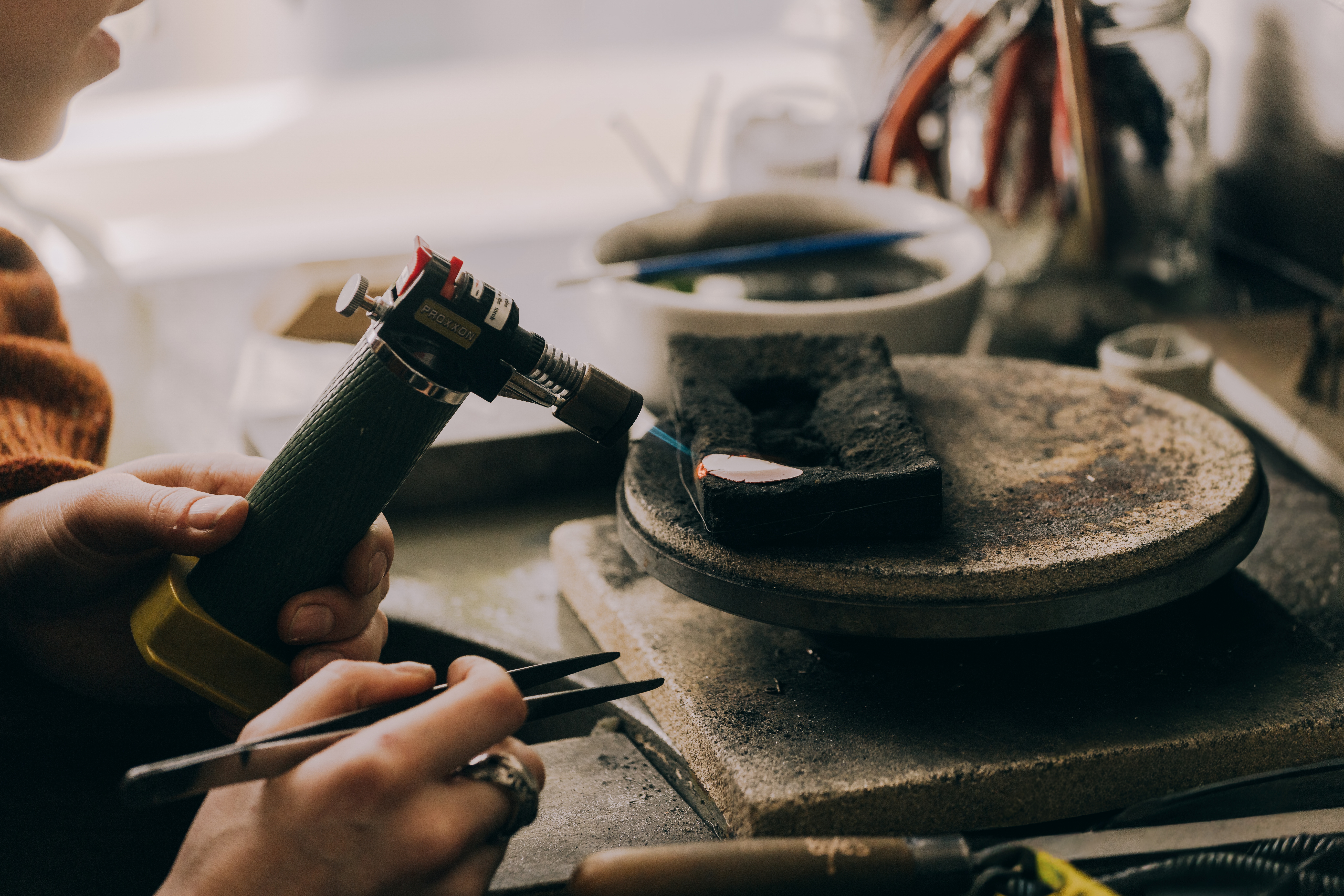 An artisan heating up a leaf of metal on her workstation.