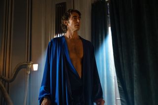 a man in a blue robe stands in front of a window with the curtains drawn