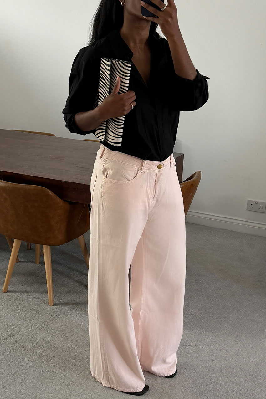A woman wearing a black button-down, pink jeans and a zebra print clutch.