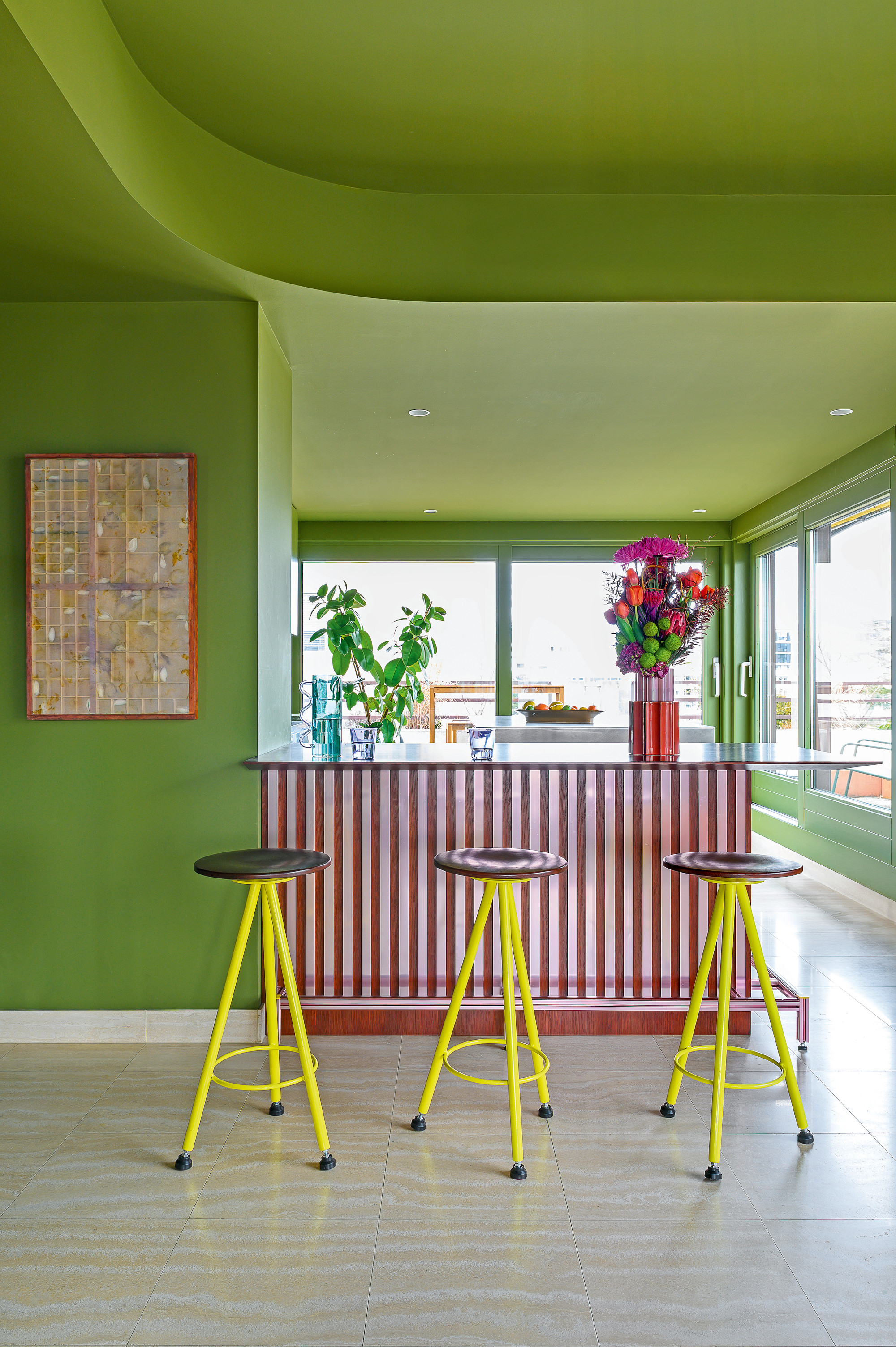 Bar area with pink and red striped bar, neon yellow bar stools, matcha green walls and red-framed pink abstract artwork