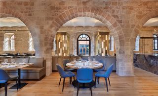 Restaurant, light wood table tops with grey seating, stone walls and light wooden floors