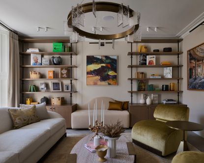 sitting room with wooden bookcases, cream sofa, green velvet chairs and statement light and artwork 