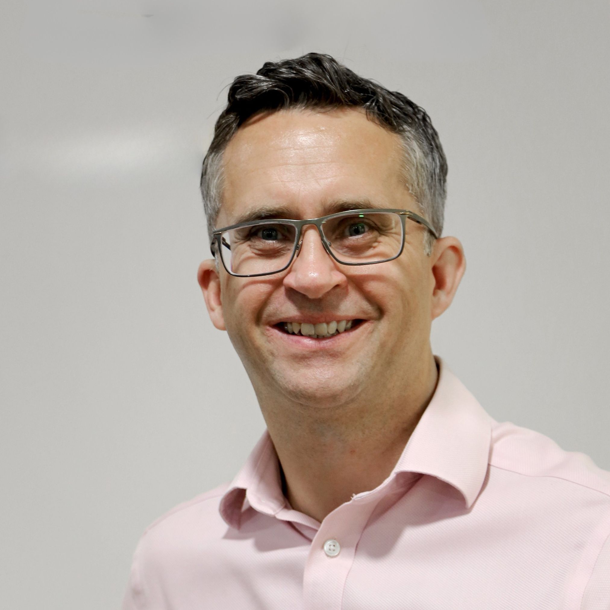 male with short grey hair wearing glasses and pink shirt