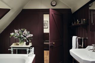 An aubergine colored bathroom in a loft space with wooden panelling and white sanitaryware