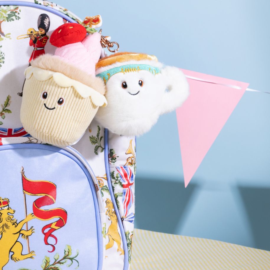 Plushies from King Charles's Royal Collection Trust Shop including a pink strawberry cupcake toy keyring and a white cuddly cup keyring on a regal backpack