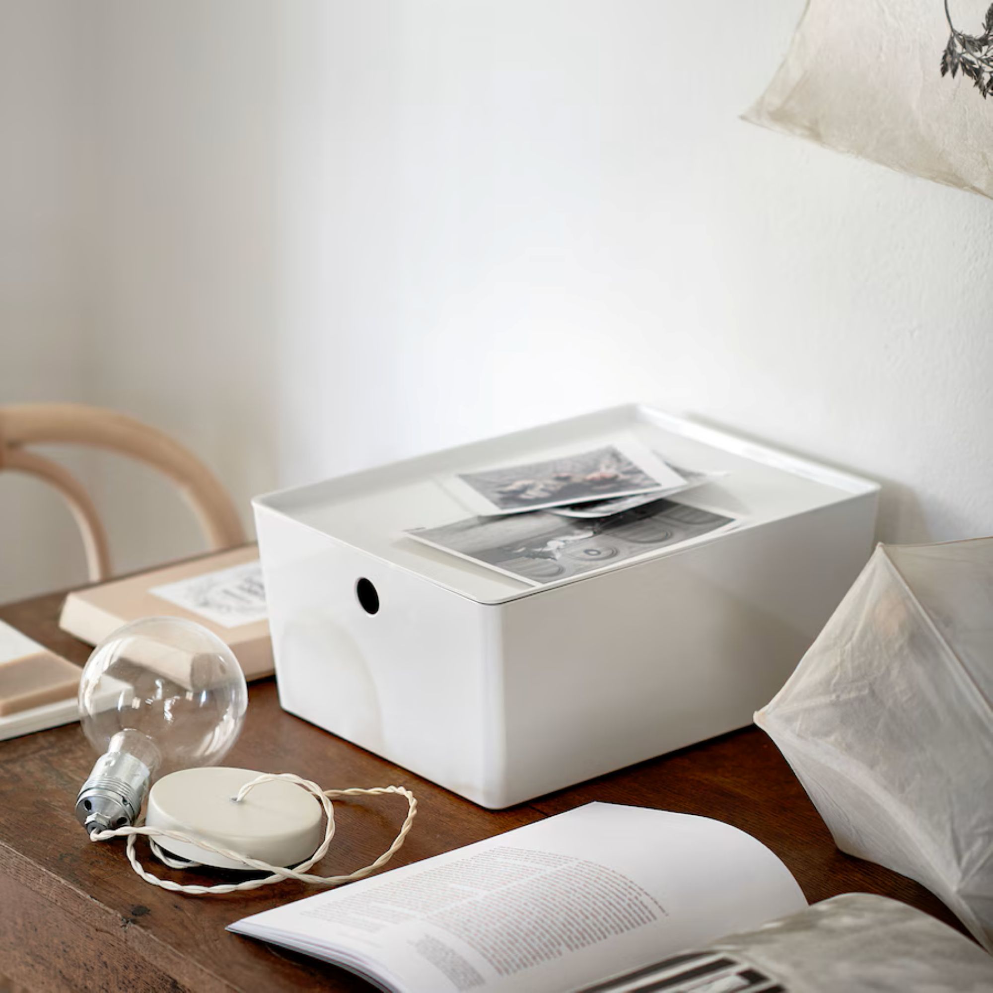 white storage box with a lid on a wooden table with an open book and a glass lightbulb