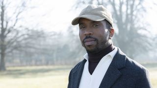 Kiell Smith-Bynoe wearing a light cap and white shirt and dark jacket standing outside as Mike in Ghosts.