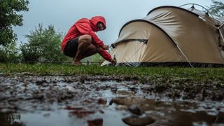 how to camp in the rain: a man setting up his tent in the rain