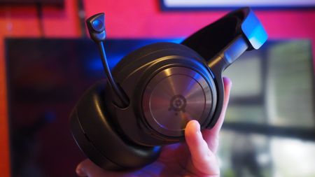 A hand holds a sleek black over-ear headset with a visible microphone against a blurred background. The mood is modern and tech-focused.