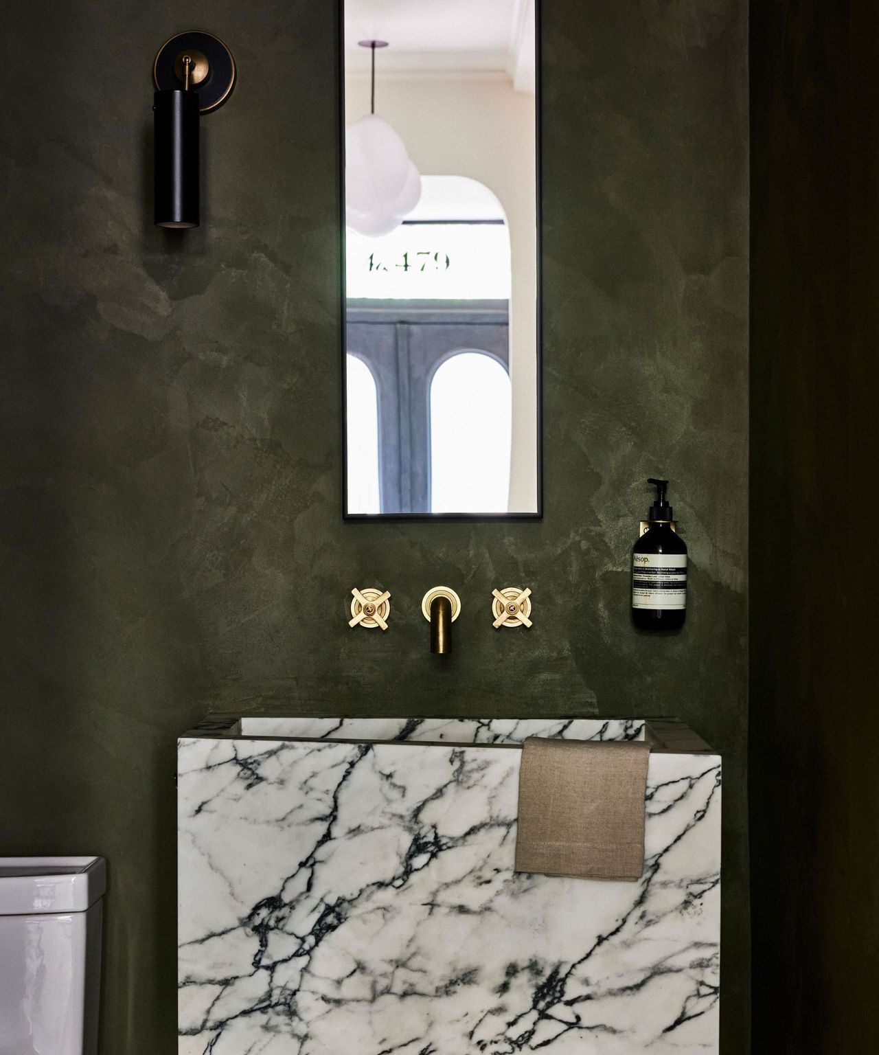 A dark green powder room with an angular black and white marble sink