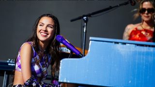 A beaming Olivia Rodrigo performs on the Other Stage while sat in front of a piano at Glastonbury 2022.