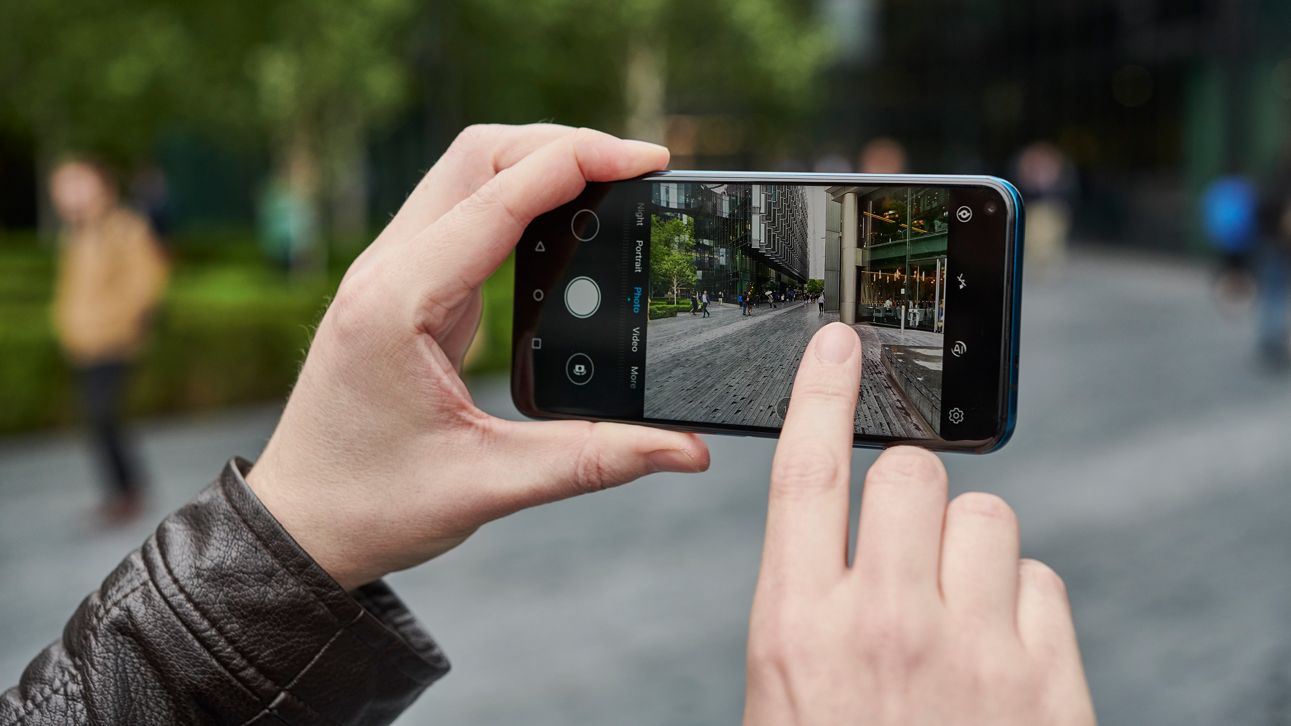 Person holding a smartphone and taking a photo of an urban street scene with buildings and pedestrians