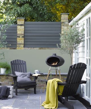 A green and black painted garden boundary with an outdoor fire and deck chairs