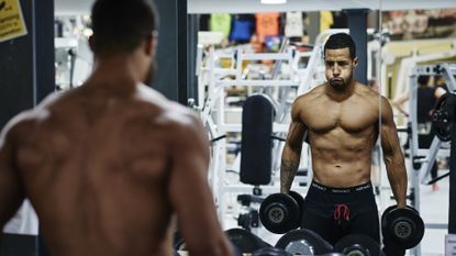 Determined muscular guy looking in the mirror in the gym before his dumbbell workout commences