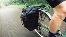 A black pannier mounted to a green bike with the background motion blurred