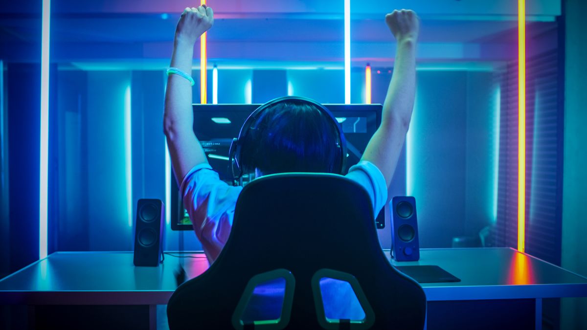 A PC gamer celebrating, sat in a gaming chair in front of a monitor