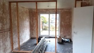 Room with bare plaster walls, french doors and part built timber stud wall