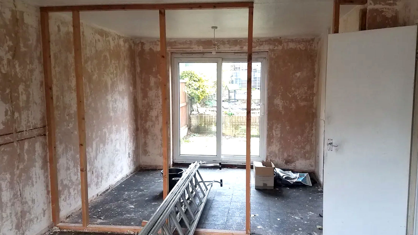 Room with bare plaster walls, french doors and part built timber stud wall