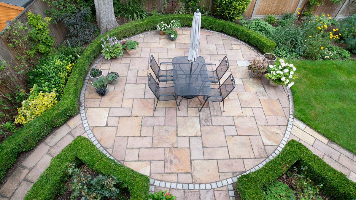 A circular patio with table, chairs, umbrella and plants