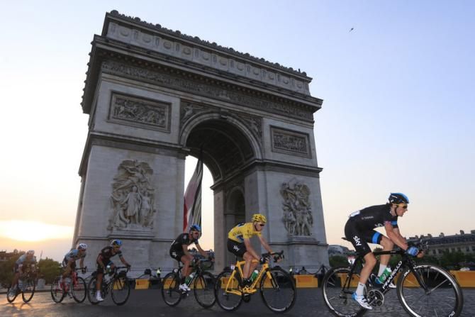 The peloton passes the Arc de Triomphe as daylight falls over Paris