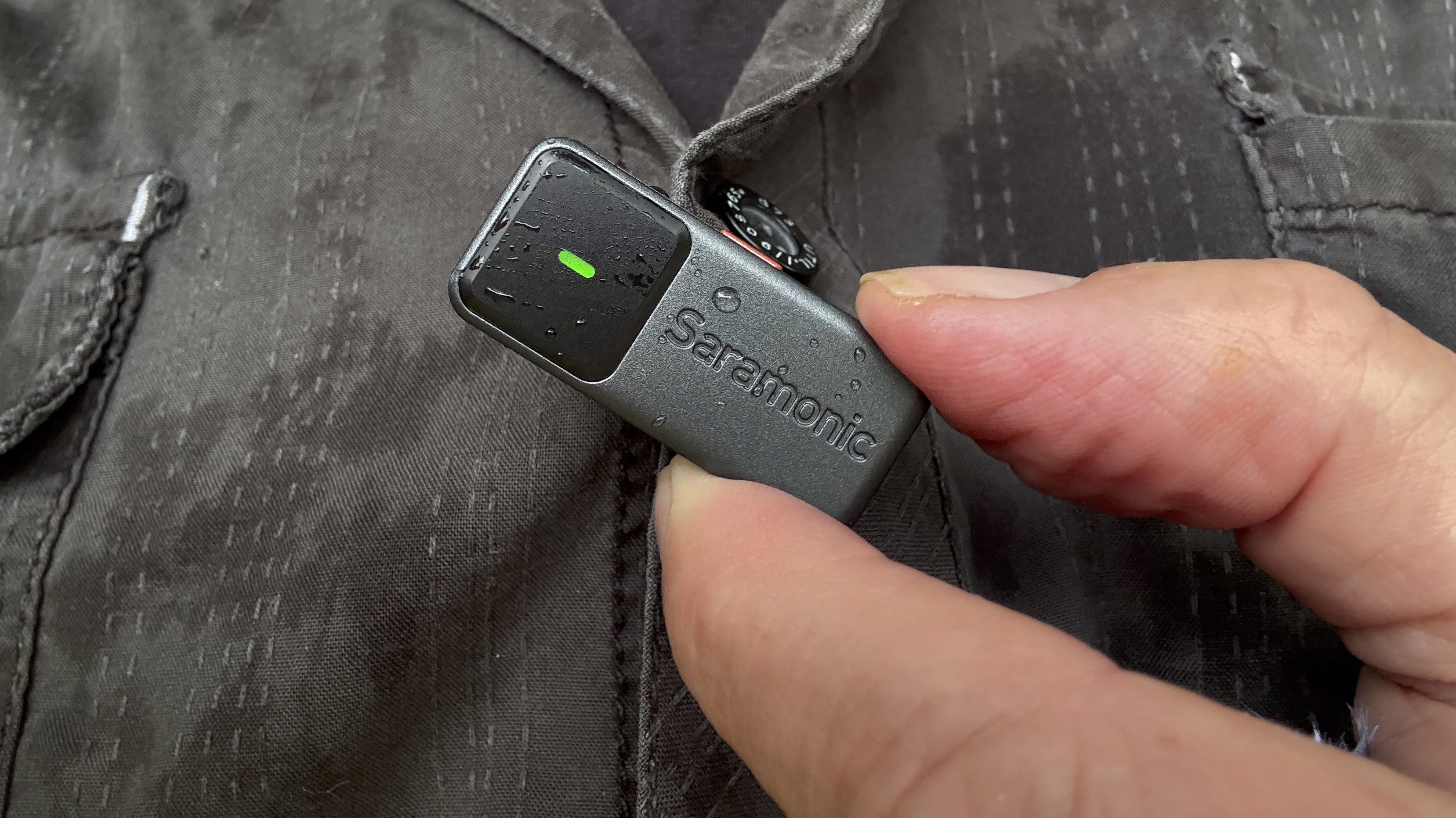 Close-up of a hand holding the transmitter mic. The status light on the mic is green to indicate that its built-in noise reduction feature is active