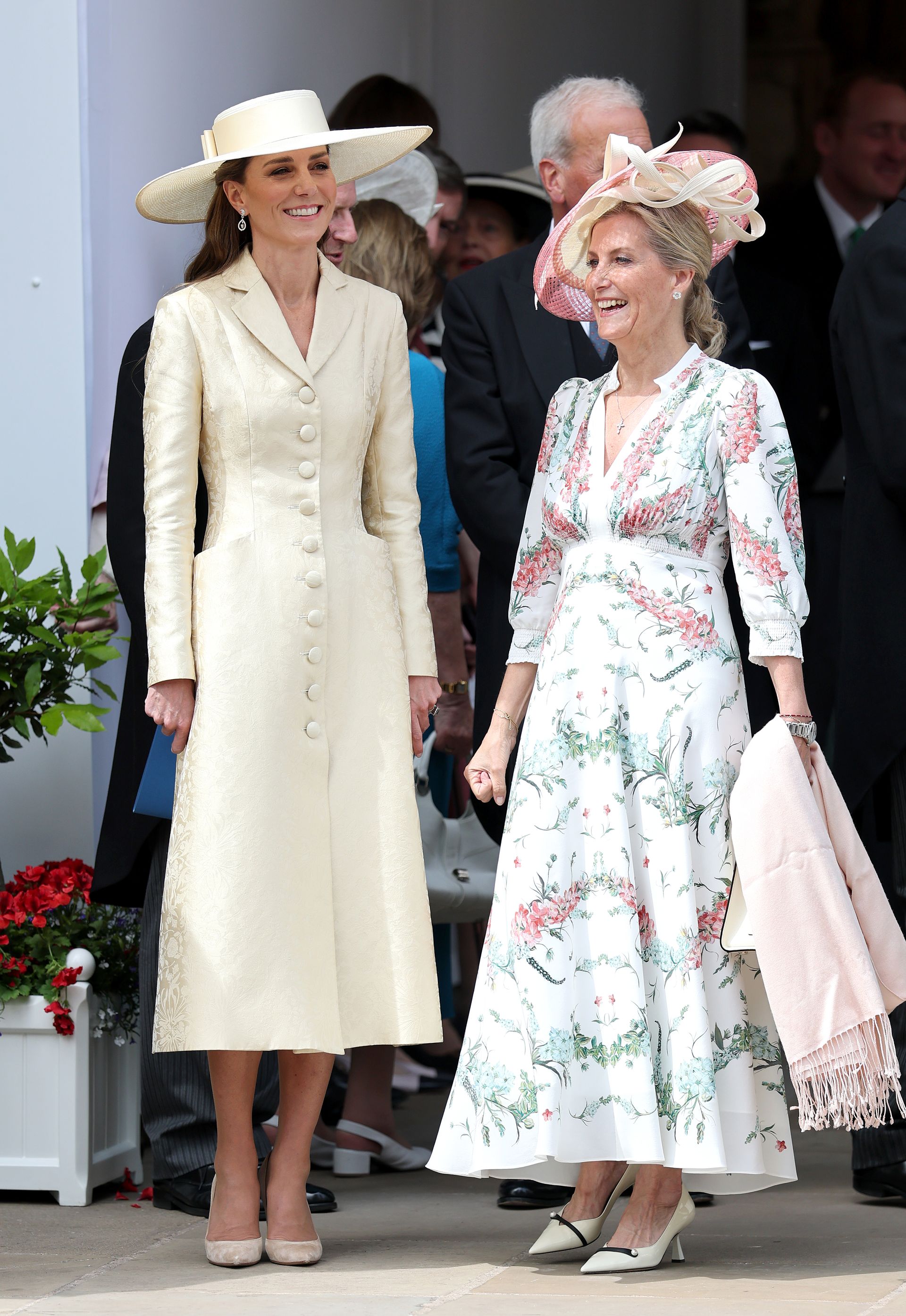 Kate Middleton wears a butter yellow coat dress with beige heels and a yellow wide-brim hat.