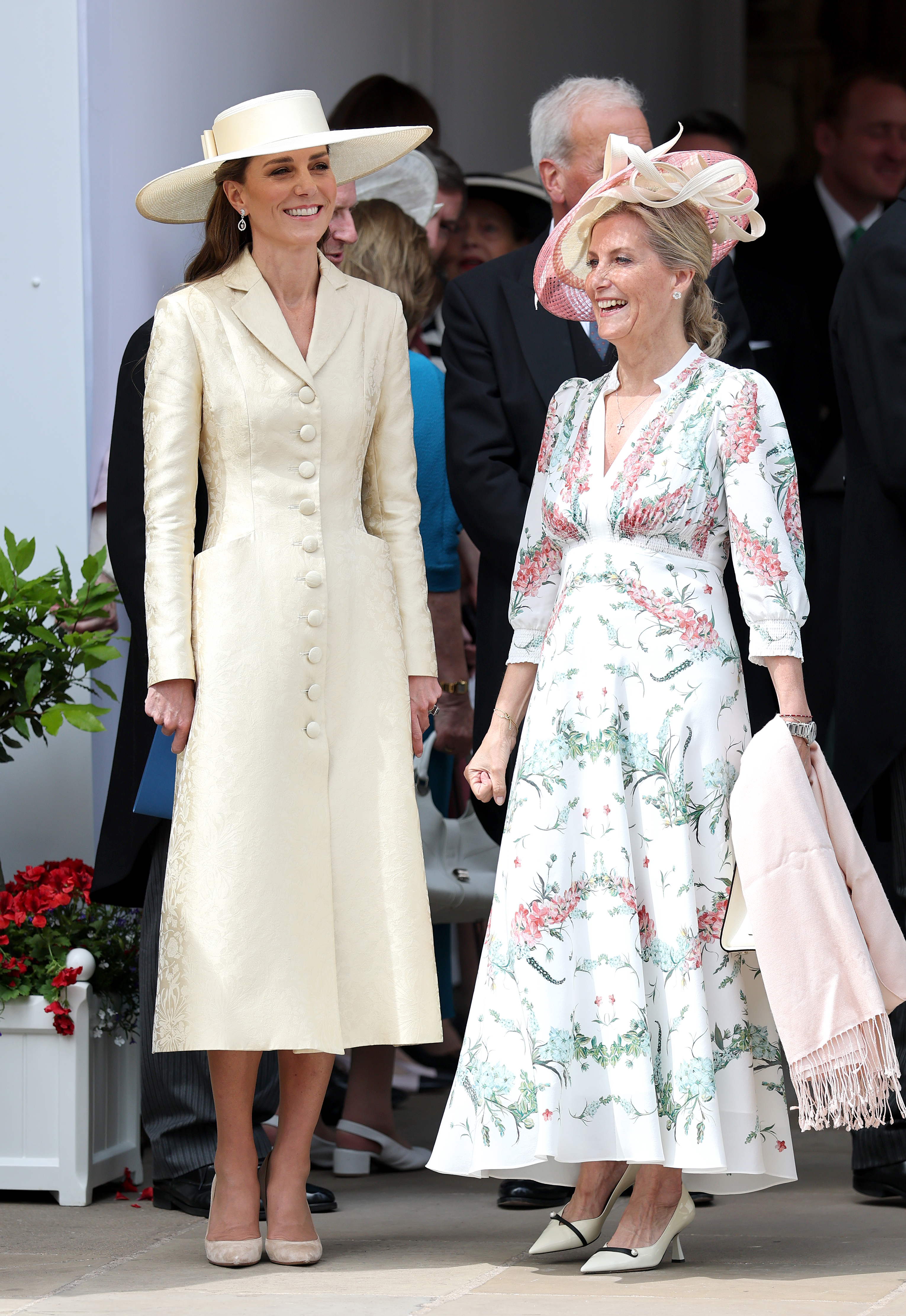 Kate Middleton wears a butter yellow coat dress with beige heels and a yellow wide-brim hat.