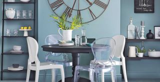 Pale blue dining room with large industrial-style wall clock and black round dining table