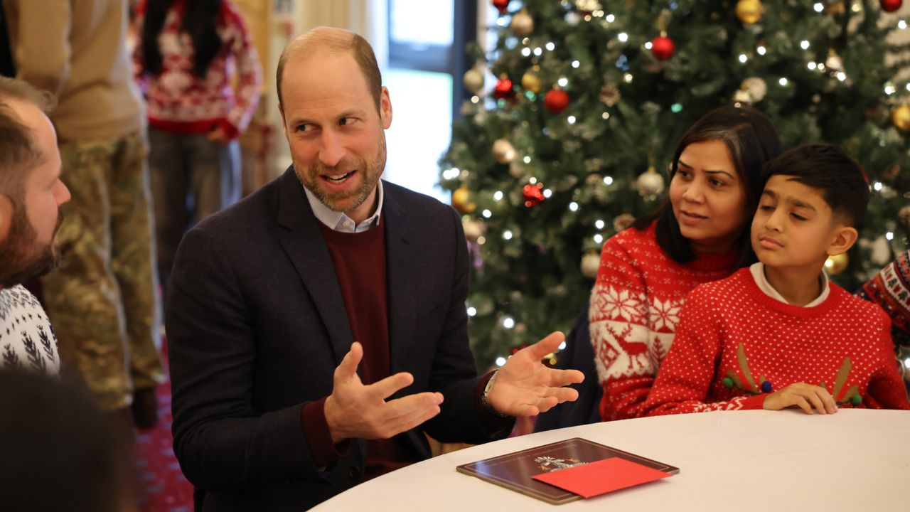 Prince William talking to people wearing Christmas sweaters at a table