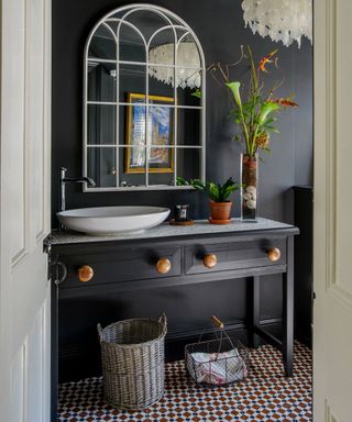 A cloakroom with a black painted wall and a large mirror above a white basin on a gray vanity