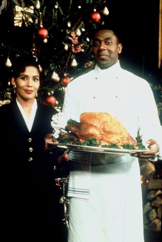 a woman poses by a chef in a white outfit holding a turkey in the british tv show chef