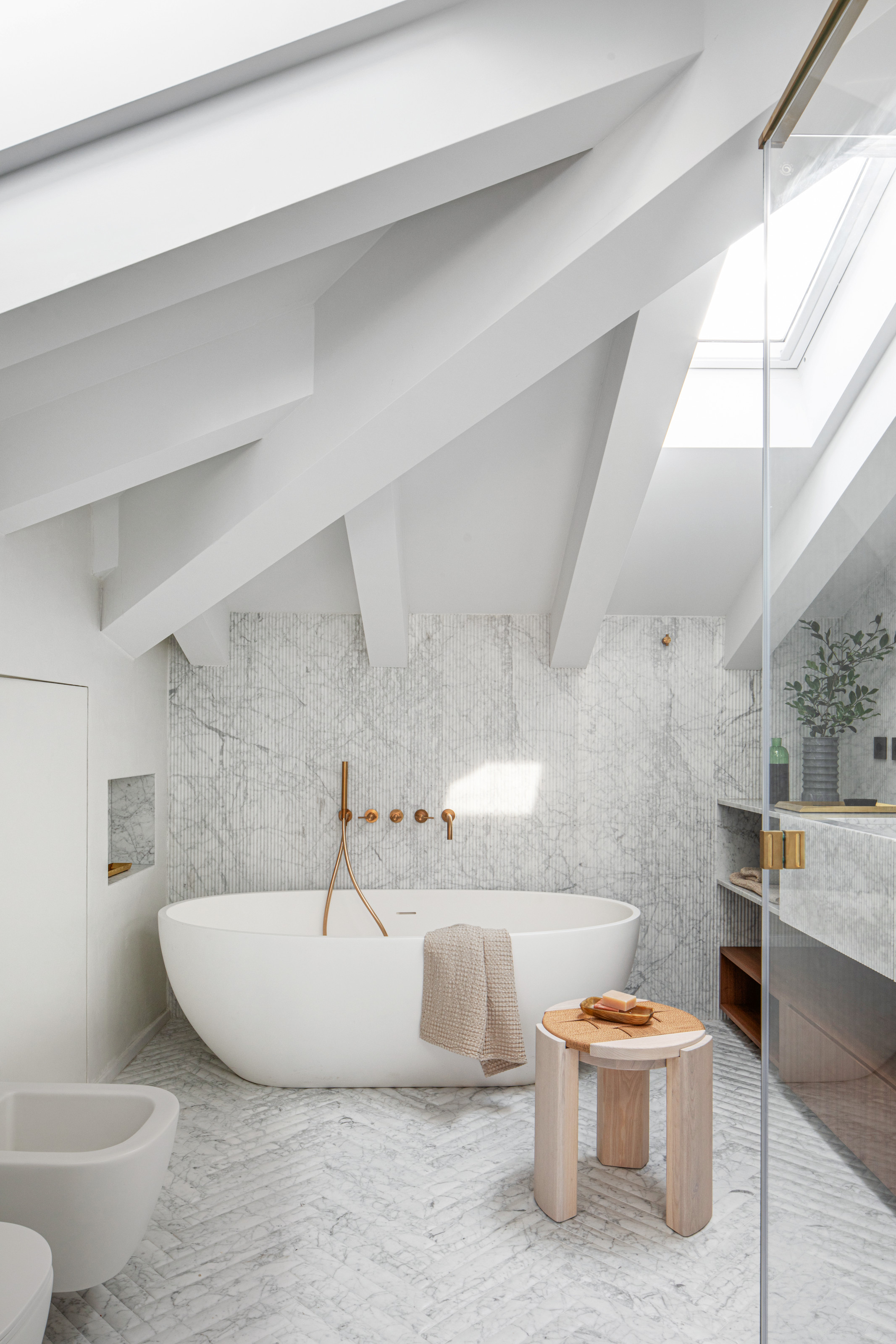 White bathroom with diagonal ceiling beams, contemporary white freestanding bath and pale wood stool