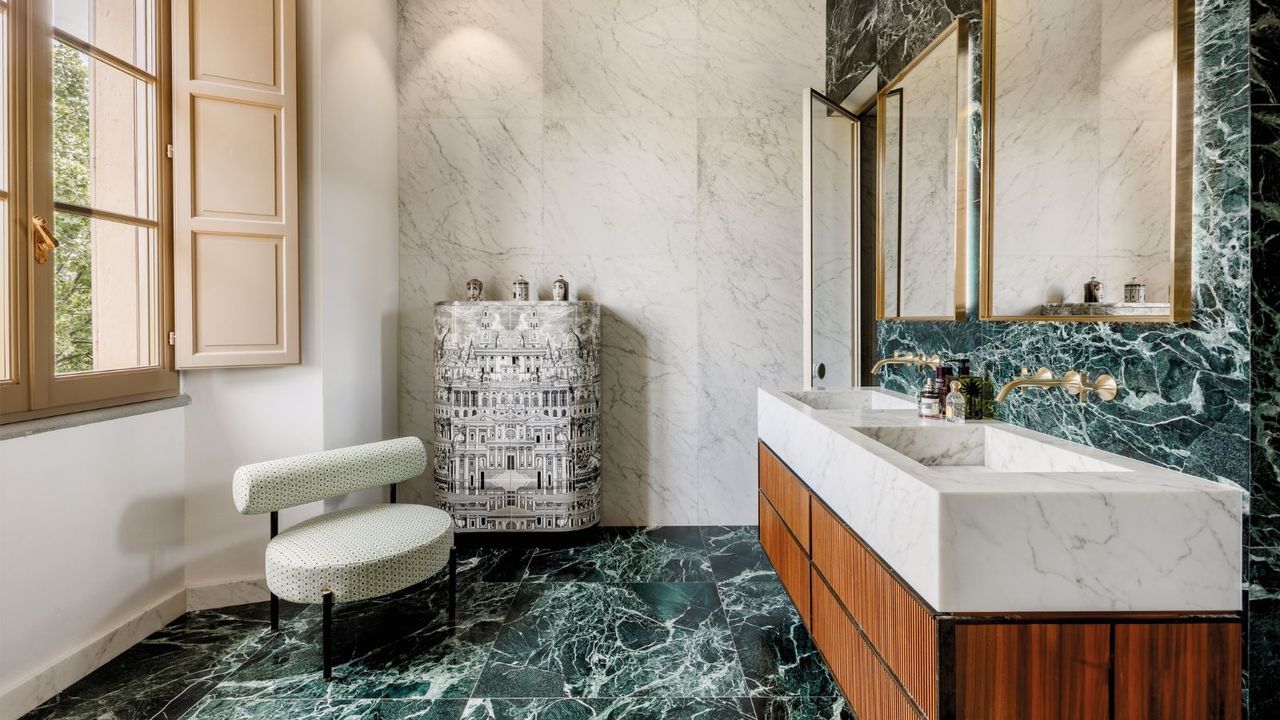 A luxurious bathroom combining white and green marble, a fluted wood vanity and brass fittings for a bold yet elegant, design-led look.