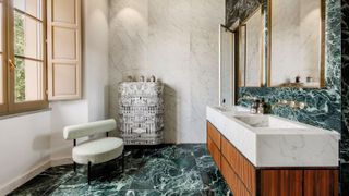 A luxurious bathroom combining white and green marble, a fluted wood vanity and brass fittings for a bold yet elegant, design-led look.