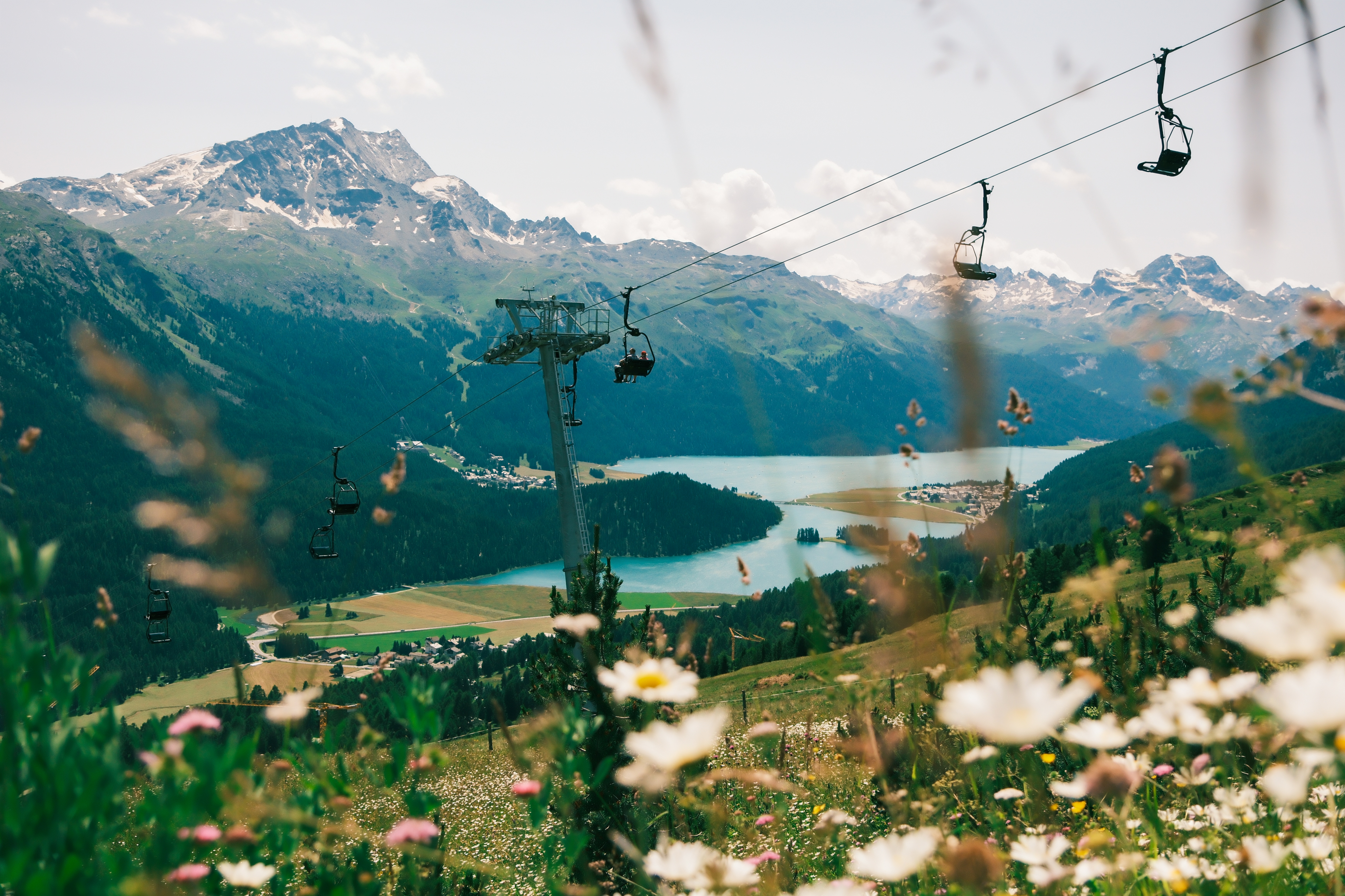 A ski lift, situated atop a lush, blooming natural reserve encircling a moutain lake, is captured in spring while bathing in the sunshine.