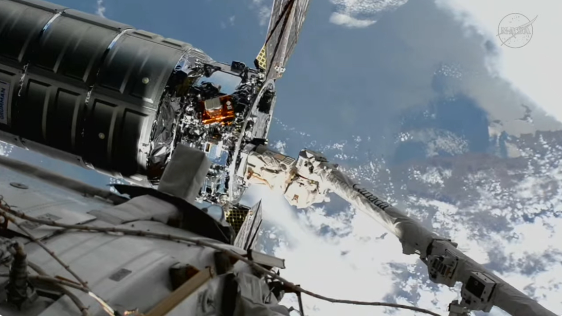a spacecraft is held by a robot arm over Earth