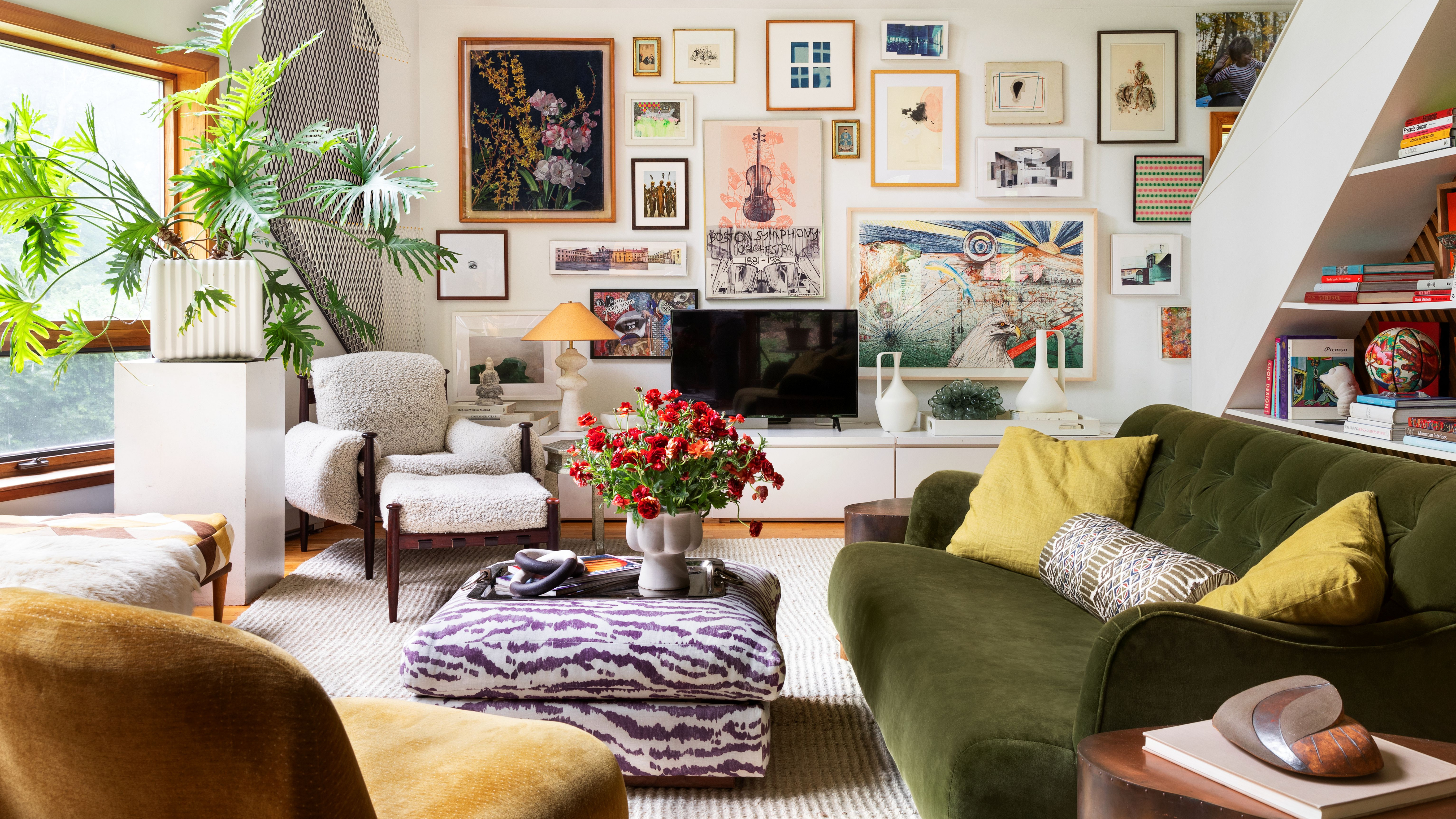 Eclectic sun drenched living room featuring a zebra patterned ottoman and cozy upholstered sofas and chairs. The far wall features a credenza styled with various sculptural objects. Above, there is a gallery wall of assorted paintings and prints. 