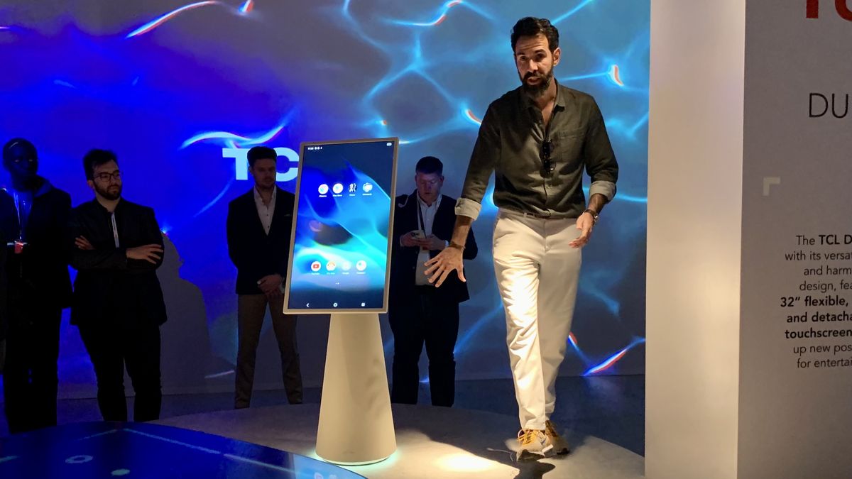 TCL Dune TV on a stage at Milan Design Week, with a man standing next to it