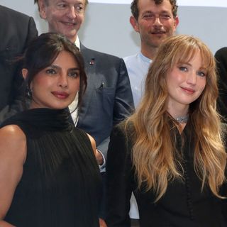Jennifer Lawrence has long blonde hair and is wearing a black Dior suit, Priyanka Chopra wears her black hair tied back and wears a black Dior dress with a white tiered skirt
