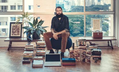 Julián Fuks sitting on a chair with books on the floor 