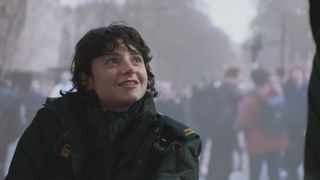 Naomi Wakszlak as trainee paramedic Indie Jankowski in Casualty 2025, wearing full paramedic green uniform and smiling at someone off screen.