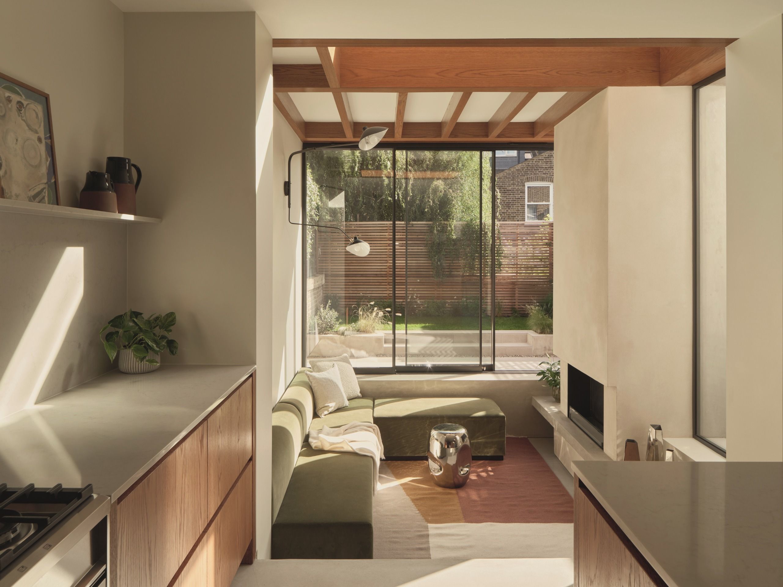 conversation pit in modern extension with fireplace, exposed timber ceiling details, galley kitchen, and L-shaped sofa