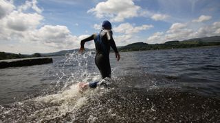A swimmer in a wetsuit runs into the water