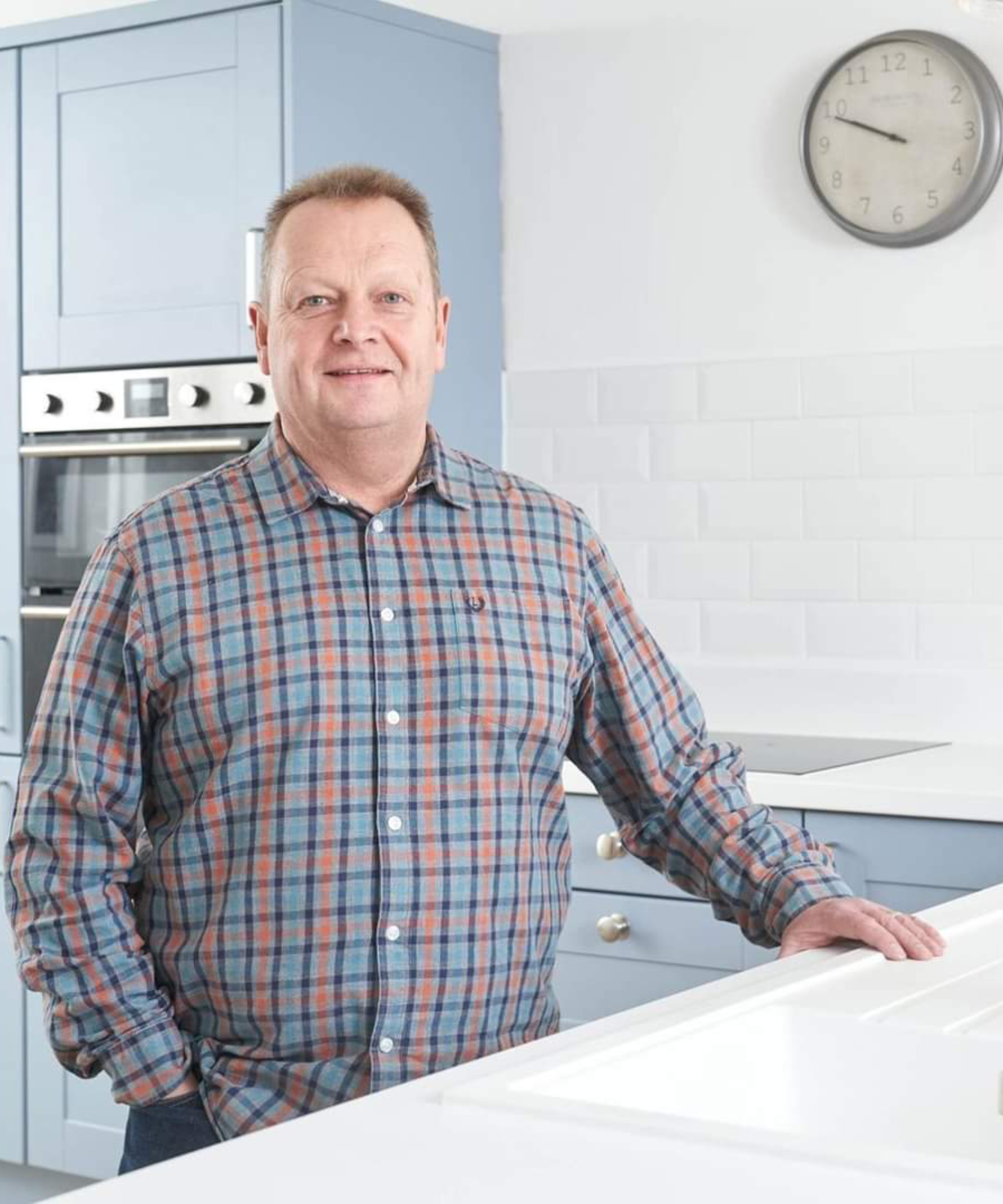 headshot of male wearing checked shirt stood in kitchen