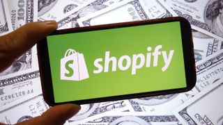 A hand holding a phone with the Shopify logo